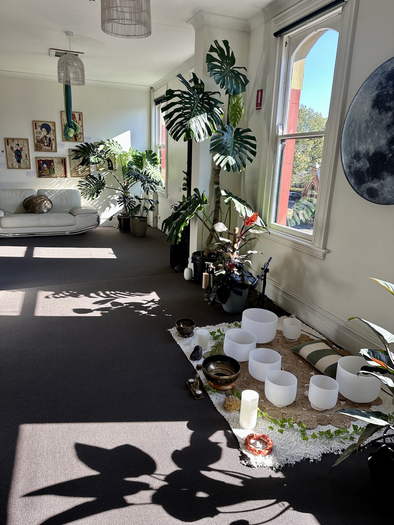 Sunlit Mystic Wellness studio rental space with moon wall, plants, windows, and singing bowls in Petersham